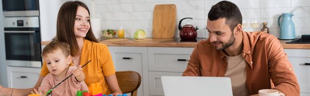 Mãe e filho com pincel sentado perto do marido com laptop, banner  - Foto, Imagem