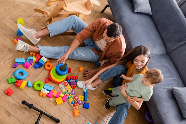 High angle view of smiling mother hugging son near husband and games at home  - Fotoğraf, Görsel