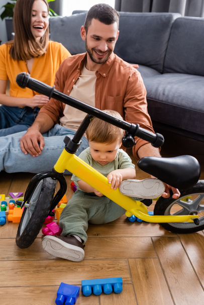 Kid looking at bike near parents and building blocks at home  - Foto, imagen