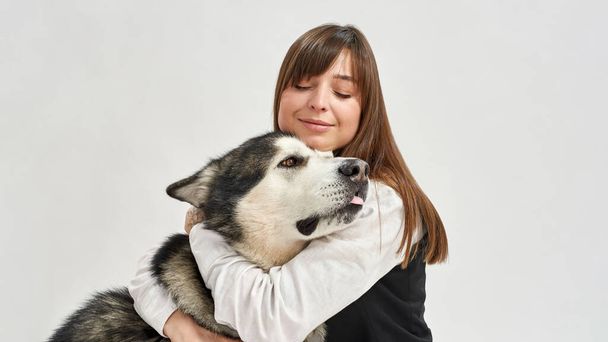Girl hugging Siberian Husky dog in white studio - Фото, изображение