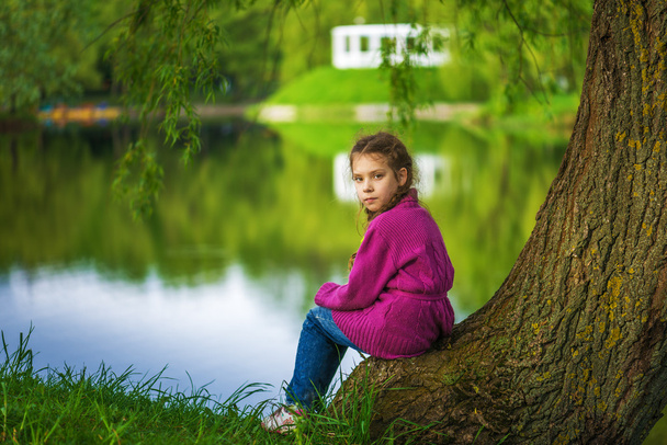 Little girl sits near lake - Φωτογραφία, εικόνα