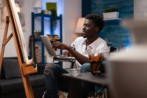 African american artist holding laptop searching for painting inspiration - Photo, Image