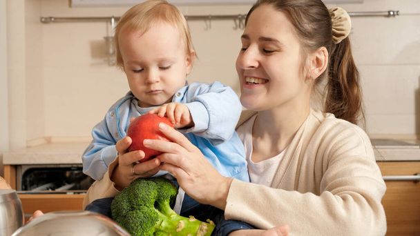 Young mother showing kitchen cookware, utensils and ingredients to her baby son on kitchen. Concept of little chef, children cooking food, good family time together. - Foto, Bild
