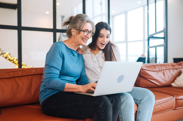 Mother and daughter sitting on couch and watching something on laptop - Photo, Image