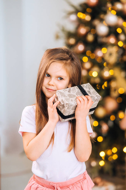 Charming little girl holds a gift on a background of Christmas trees - Photo, Image