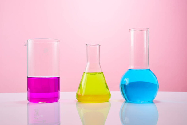 Different laboratory glassware with color liquid on a pink background. Test tubes with colorful liquids for laboratory chemical research. - Foto, Imagen