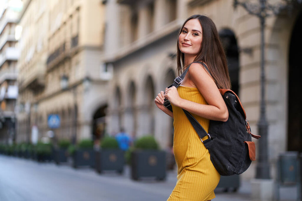 όμορφη νεαρή γυναίκα διασχίζει ένα δρόμο, με το σακίδιό της στην πλάτη της - Φωτογραφία, εικόνα