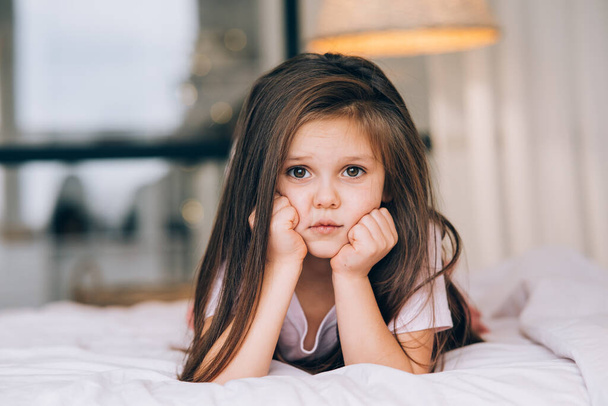 Nettes kleines Mädchen mit traurigem Gesicht auf dem Bett liegend - Foto, Bild