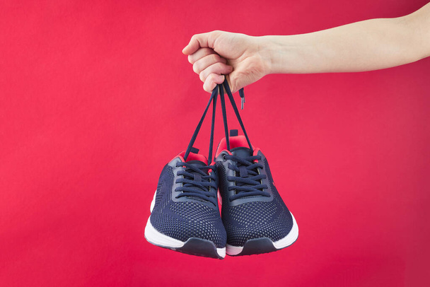 Hand hold sports shoes on a red background. Holding new fashion sneakers for running. Choosing and buy of new sneakers. - Foto, Bild