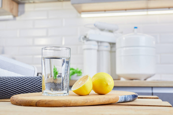 Glass of clean filtered water with lemon and ice in kitchen. Breakfast and fresh morning drink. - Foto, afbeelding