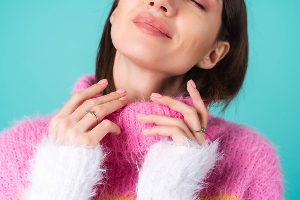 Close portrait of a young woman in a sweater on a blue background with graceful hands, long thin fingers, two cute silver rings, plump nude lips - Photo, Image