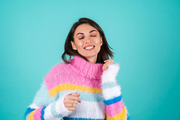 Young woman in a bright multicolored sweater on a blue background, smiles, moves cheerfully, dances alone - Photo, Image