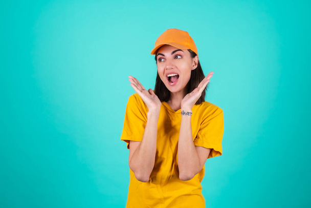 Mladá žena poslíček, kurýr, v oranžové žluté čepici na modrém pozadí šokované překvapené výkřiky - Fotografie, Obrázek