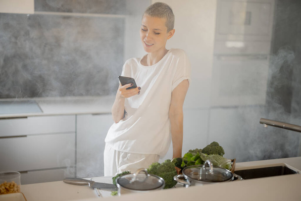 Woman using phone before cooking vegetarian dish - Foto, Bild