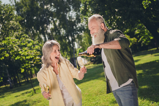 Photo of retired pensioner husband wife people drink champagne anniversary crazy mood bottle glass outside outdoors in park - Foto, Imagen