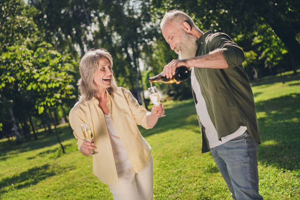 Kuva positiivinen eläkkeellä osapuoli pari mies pidä pullo kaada samppanjaa lasi kulumista rento asu luonnonpuisto puutarha ulkopuolella - Valokuva, kuva