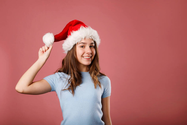 Young happy woman in Santa Claus hat standing over pink background. Copy Place for your text. Christmas and New year concept. - Photo, image