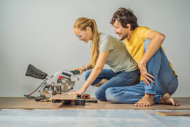 Married couple installing new wooden laminate flooring on a warm film floor. Infrared floor heating system under laminate floor - Φωτογραφία, εικόνα