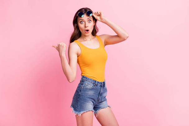 Photo of funky impressed young lady dressed yellow tank-top dark glasses pointing thumb up empty space isolated pink color background - Photo, Image