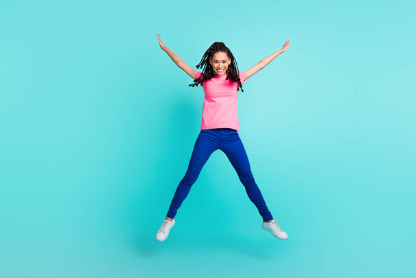 Photo of positive funny girl jump have fun raise hands wear pink t-shirt isolated on blue color background - Фото, зображення