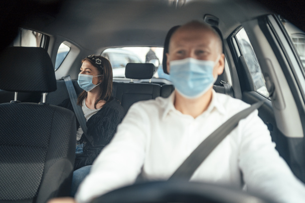Taxifahrer in Maske mit einer Kundin auf dem Rücksitz mit Maske - Foto, Bild