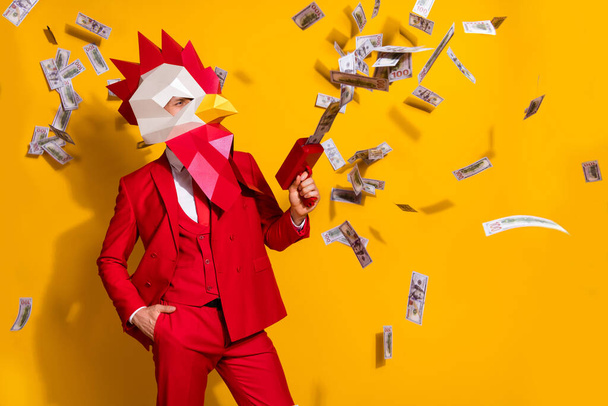 Photo of confident millionaire guy hold pistol shoot usd banknotes wear cock mask red suit isolated yellow color background - Foto, Imagen