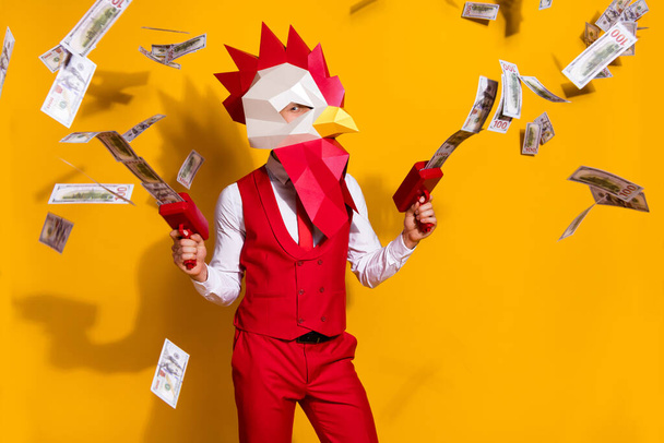 Photo of weird guy hold money gun spend million usd wear cock polygonal mask red suit isolated yellow color background - Фото, зображення