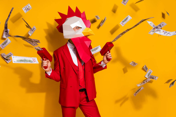Photo of funky authentic guy hold money gun shoot cash wear rooster mask red suit isolated yellow color background - Φωτογραφία, εικόνα