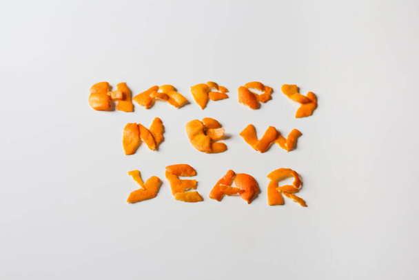 Καλή Χρονιά. Defocus Πρωτοχρονιά λέξη εμφανίζεται από πορτοκαλί ξηρό φλοιό σε λευκό φόντο. Διακόσμηση για το Νέο Έτος. Ευχετήρια κάρτα. Κείμενο και DIY γράμματα. Σύνορα και πλαίσιο. Διακοπές. Εκτός εστίασης. - Φωτογραφία, εικόνα