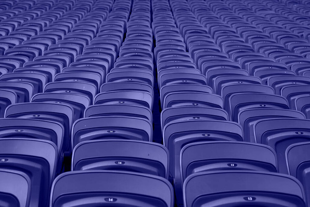 Leere rote Plastiksitze in einem leeren Stadion. Viele leere Zuschauerplätze auf den Rängen. Farbe des Jahres 2022 - Very Peri. - Foto, Bild