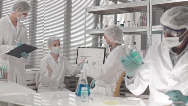 Média longa de cientistas multiétnicos ocupados vestindo vestidos médicos, máscaras e luvas, trabalhando e conversando em laboratório durante o dia - Filmagem, Vídeo