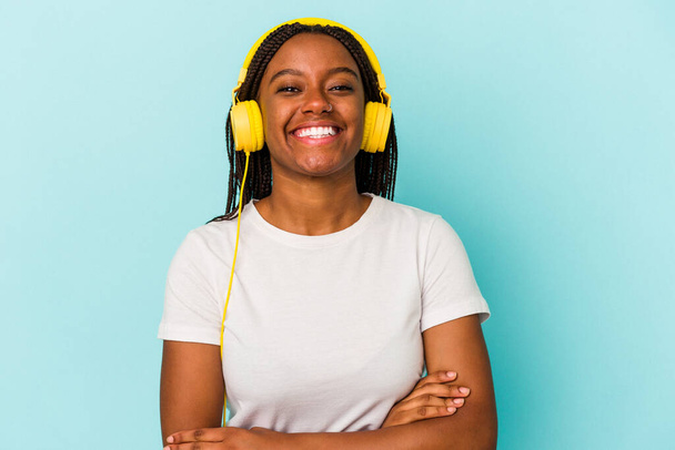 Young African American woman listening to music isolated on blue background  laughing and having fun. - Fotó, kép