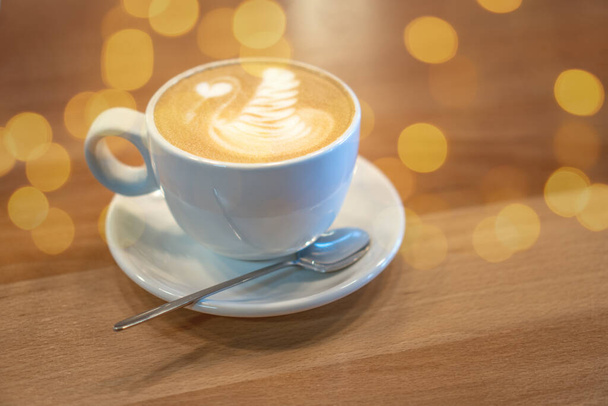 Tasse blanche de café avec latte art debout sur une table en bois dans un café. Cappuccino avec décoration au lait. Petit déjeuner matinal - Photo, image