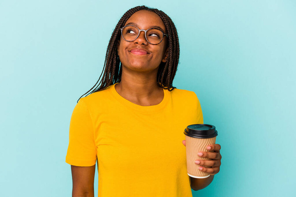 Młoda Afroamerykanka trzymająca kawę na niebieskim tle marząca o osiągnięciu celów - Zdjęcie, obraz