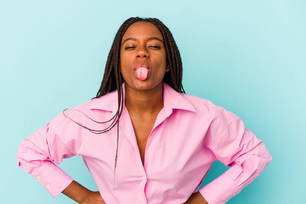 Young african american woman isolated on blue background  funny and friendly sticking out tongue. - Photo, Image