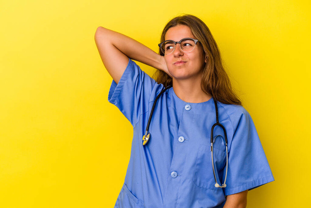 Young nurse woman isolated on yellow background  touching back of head, thinking and making a choice. - Fotografie, Obrázek