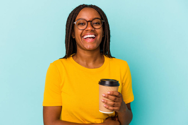 Νεαρή Αφρο-Αμερικανίδα που κρατάει καφέ μακριά απομονωμένη σε μπλε φόντο γελώντας και διασκεδάζοντας. - Φωτογραφία, εικόνα
