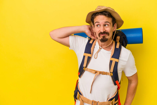 Young caucasian hiker man isolated on yellow background touching back of head, thinking and making a choice. - Photo, Image