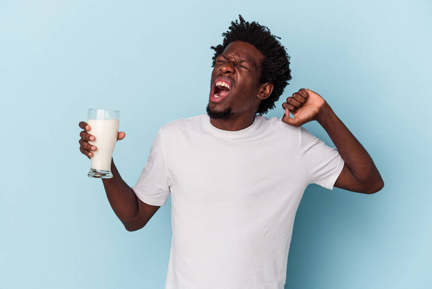 Nuori afrikkalainen amerikkalainen mies tilalla maito lasi eristetty sinisellä pohjalla - Valokuva, kuva