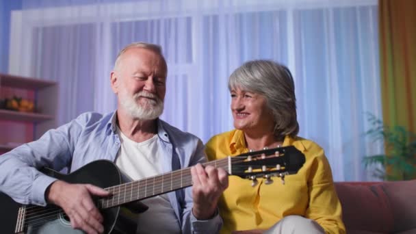 Yaşlı beyaz çift evde gitar çalarak eğleniyor. Emekli insanlar müzik aletleriyle eğleniyor. - Video, Çekim
