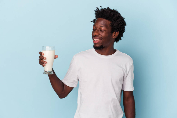 Nuori afrikkalainen amerikkalainen mies tilalla maito lasi eristetty sinisellä pohjalla - Valokuva, kuva