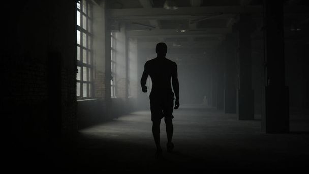 Man silhouet loopt in donkere gang. Atleet die pauze neemt na de training - Foto, afbeelding