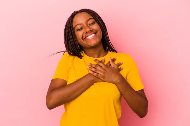 Mujer afroamericana joven aislada sobre fondo rosa tiene expresión amistosa, presionando la palma en el pecho. Concepto de amor. - Foto, Imagen