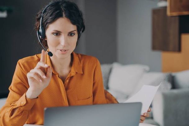 Young Spanish woman tutor wearing headset looking at laptop screen during online class - Photo, Image