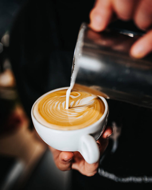 Professional barista pours white milk latte foam into a cup of coffee - the art of brewing excellent cappuccino - Photo, Image