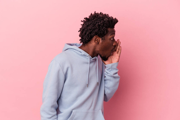 Jonge Afro-Amerikaanse man geïsoleerd op roze achtergrond zegt een geheim warm remnieuws en kijkt opzij - Foto, afbeelding