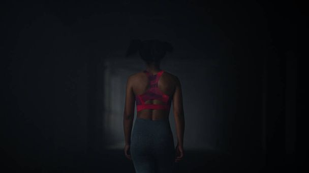 Girl walking in dark corridor. Athlete taking break after cardio workout - Фото, изображение