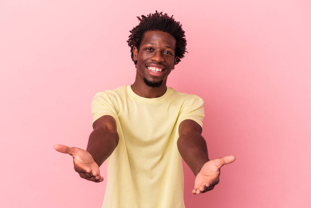 Young african american man isolated on pink background showing a welcome expression. - 写真・画像