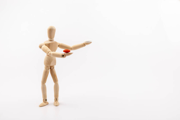 Dřevěná postava figuríny držící červenou pilulku a bílou pilulku na světlém pozadí. Koronavirus, pandemie a epidemie koncepce. Napodobení matice. - Fotografie, Obrázek