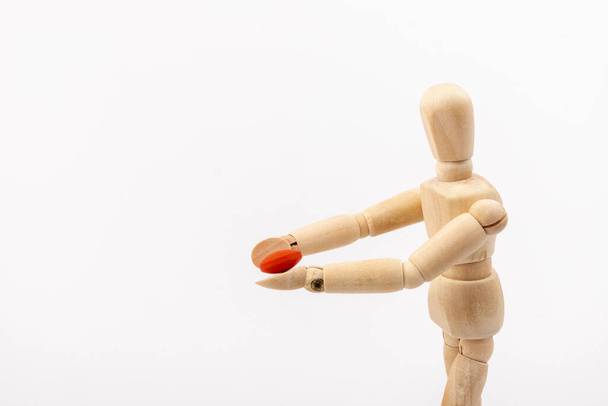Wooden ball-jointed doll holding a pill in front of its face. Concept of medicine and health - Photo, Image